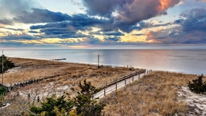 Un paysage côtier avec une plage de sable, une clôture en bois et une vue dégagée sur l’océan, le tout sous un ciel spectaculaire.