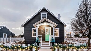 Une maison aux couleurs sombres, avec une clôture blanche en bois, une porte verte et des décorations de Noël.