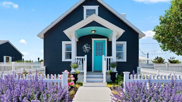 Une maison à deux étages avec une porte d’entrée de couleur turquoise, des moulures blanches et un petit porche avec des marches.