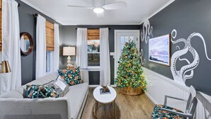 Un salon avec un canapé gris, une petite table ronde, un sapin de Noël et un mur orné d’une grande fresque représentant un poulpe.