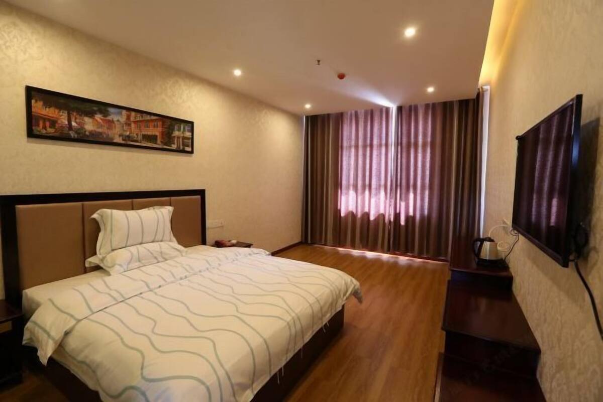 Ein Hotelzimmer mit einem großen Bett, einem Bild an der Wand, einem Fernseher und einem Fenster mit Vorhängen.