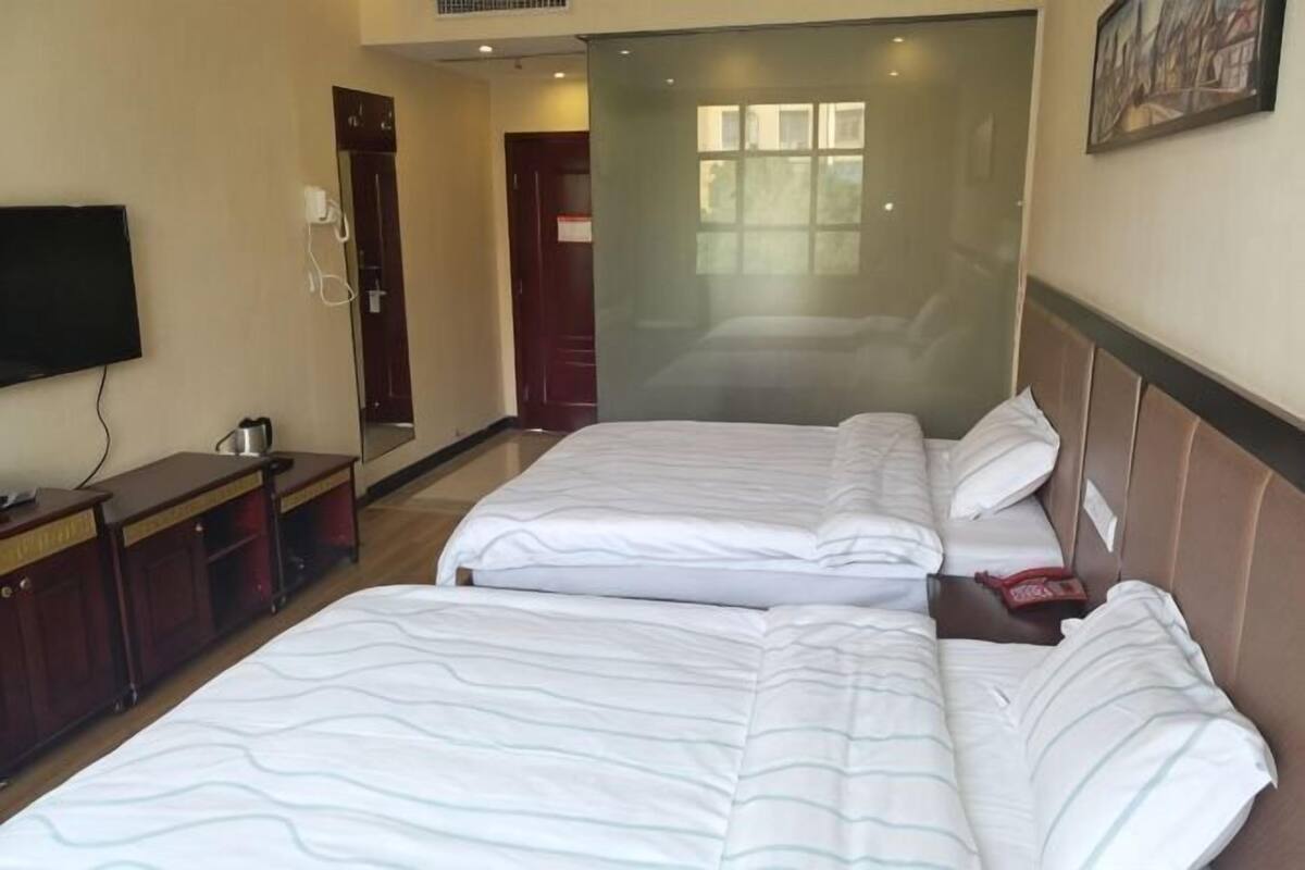 Ein Hotelzimmer mit zwei Betten, einem Fernseher, einem Schreibtisch und einem Spiegel.