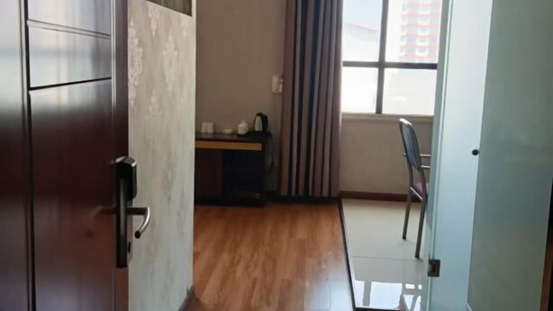 Une pièce avec un plancher en bois, un bureau avec une chaise, une fenêtre avec des rideaux et une porte.