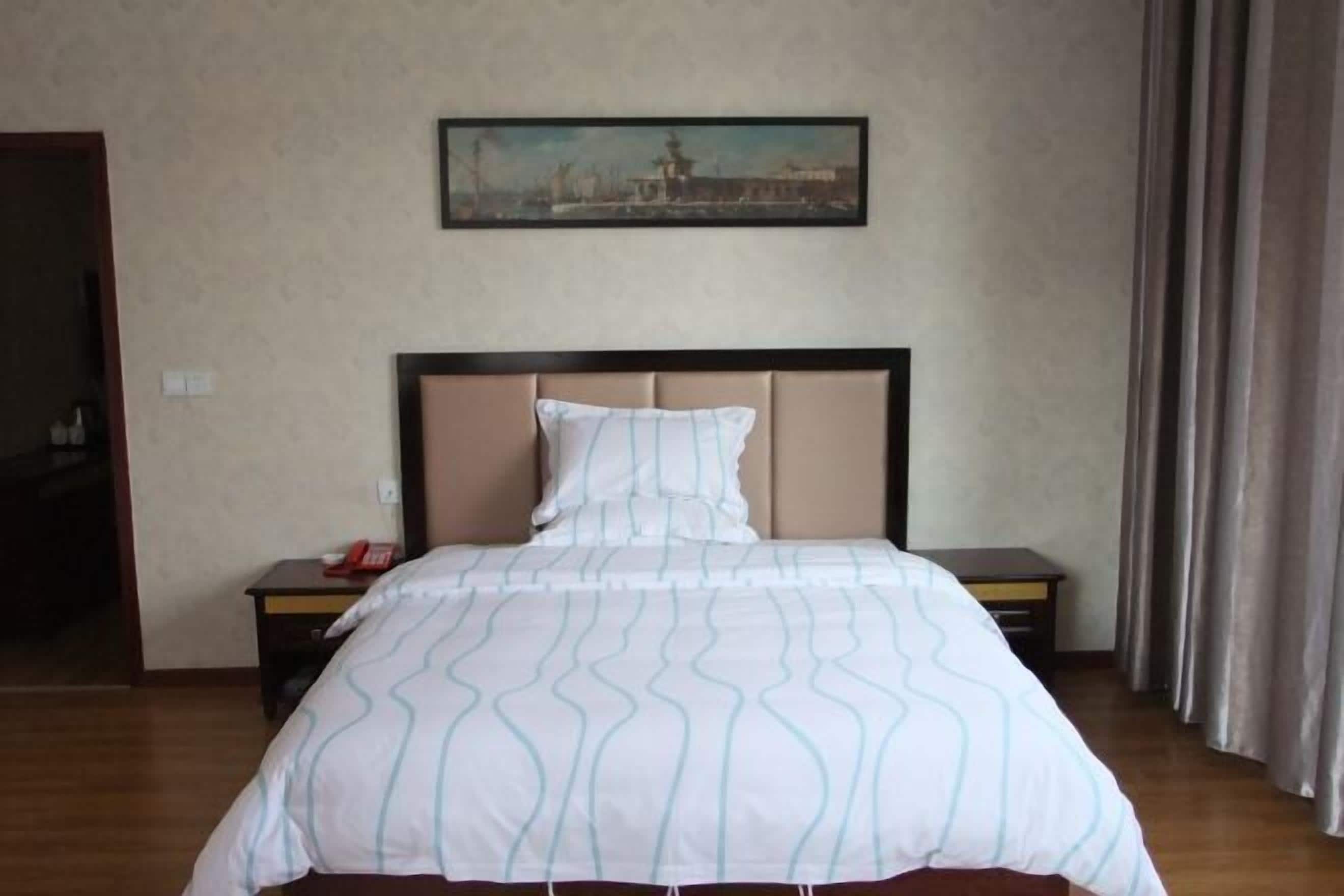 A hotel room with a bed, a nightstand, a painting on the wall, and a curtain.