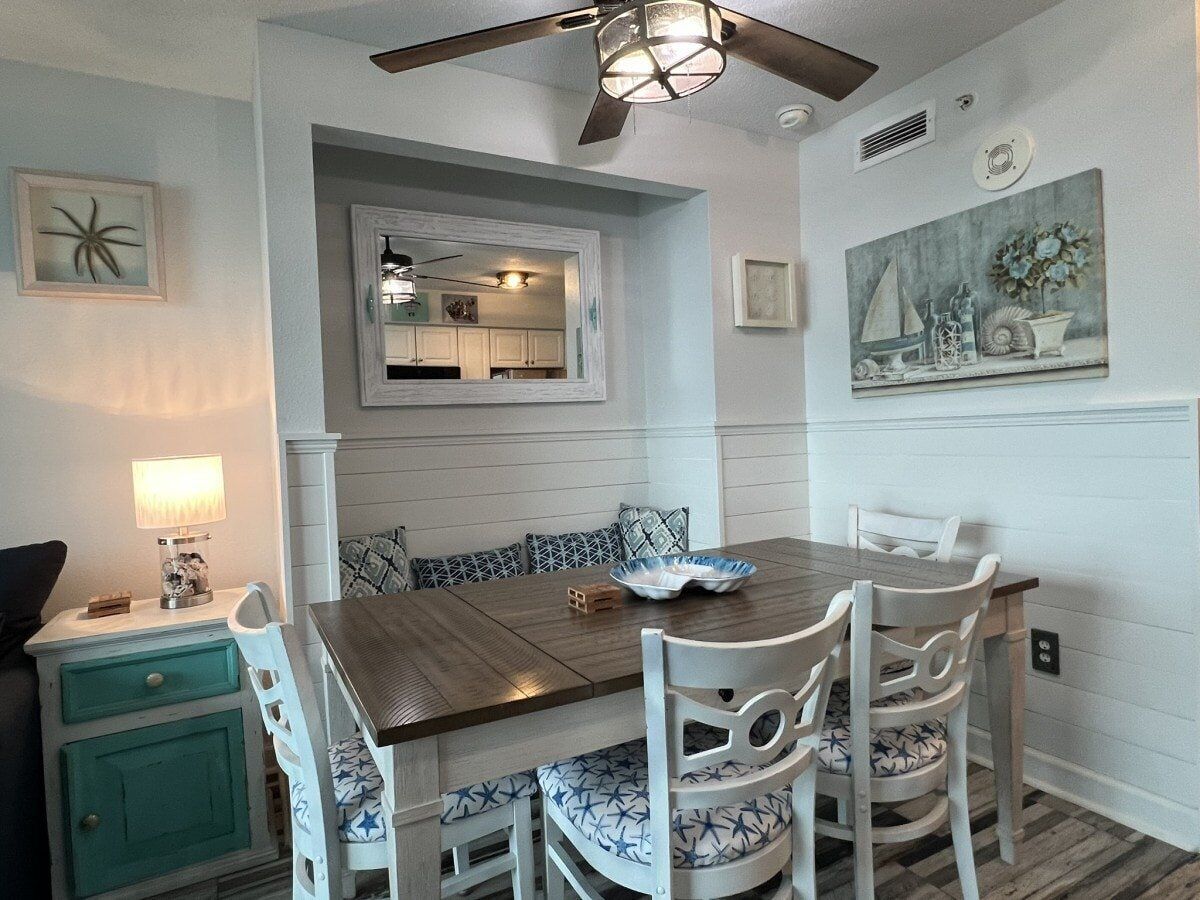 A dining area with a wooden table, white chairs, and a bench with patterned cushions.