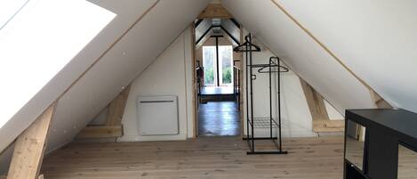 An attic room with a sloped ceiling, wooden flooring, a white radiator, a black metal rack, and a black cabinet.