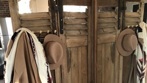 Une pièce rustique aux murs en bois, agrémentée d’un grand miroir qui reflète l’intérieur. On aperçoit une porte en bois avec une poignée en métal, et une couverture est accrochée à la porte.