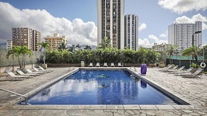 Ein Pool mit Liegestühlen, umgeben von hohen Gebäuden und Grünflächen.