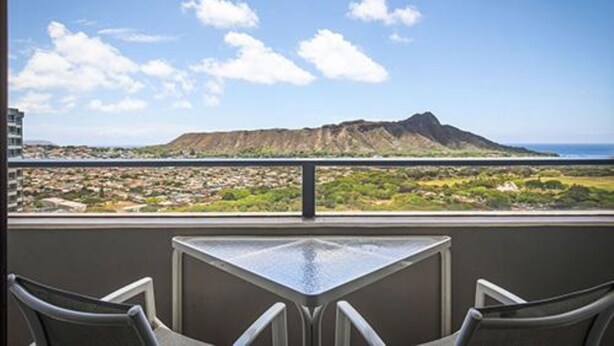 Ein Balkon mit Tisch und Stühlen mit Blick auf eine gebirgige Landschaft und eine Küstenstadt.