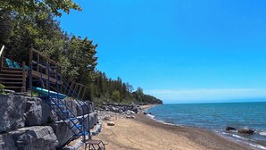 A beach with a wooden staircase leading down to the shore, surrounded by rocks and trees. - Willow Crest - Lake front with Private Lake Access (Bayfield)