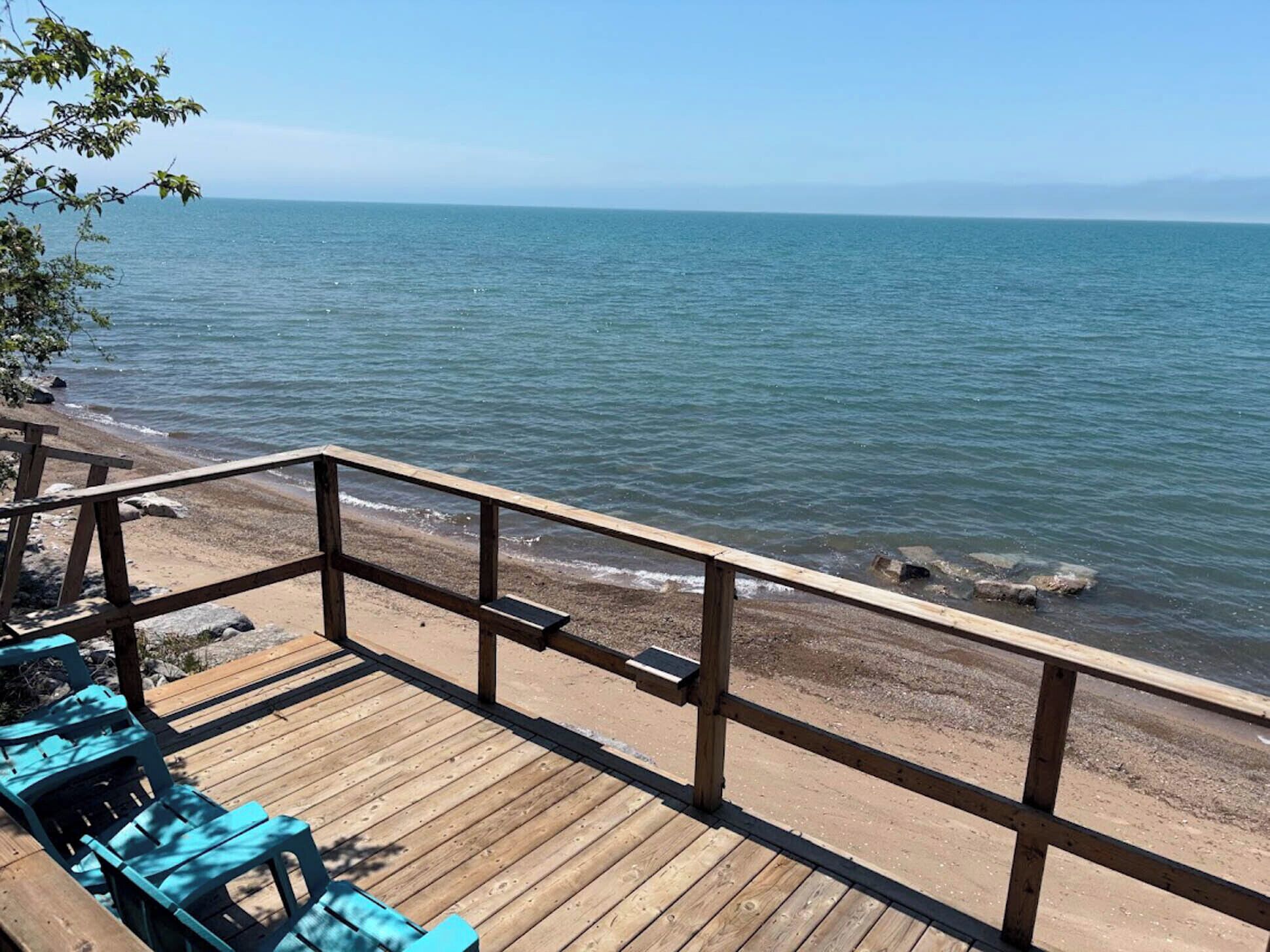 Um deck de madeira com guarda-corpo, dando vista para a praia e o mar.