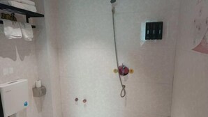 Ein Badezimmer mit Dusche, Handtuchhalter, Toilettenpapierhalter und einem an der Wand befestigten Lichtschalter.