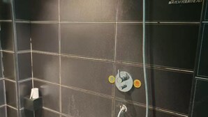 A bathroom with dark tiled walls, a hand dryer, and a showerhead. - Huiquan Holiday Hotel (Guiyang)