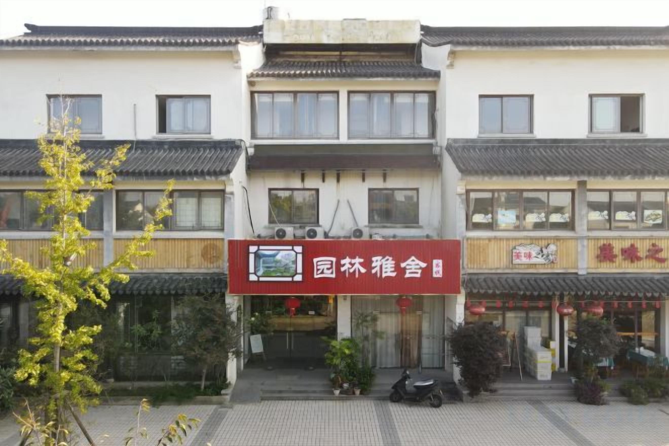 A traditional building with a signboard, a tiled entrance, and a small garden area.