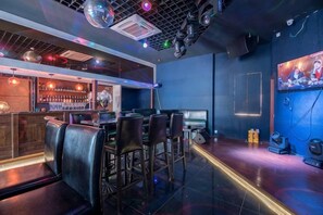 Zona de bar con barra, taburetes y una pantalla de televisión.