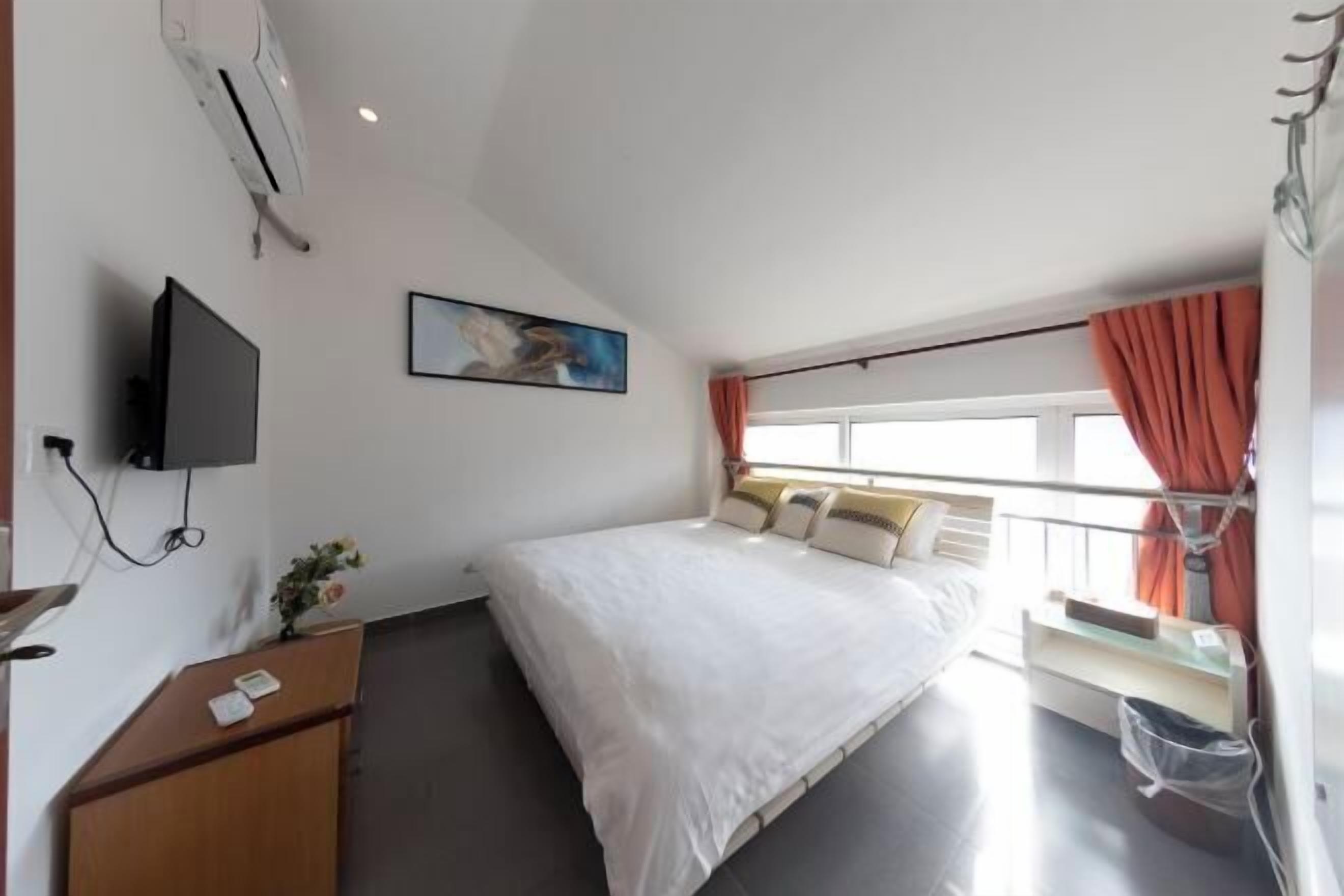 A hotel room with a bed, a desk, a TV, a window with curtains, and a painting on the wall.