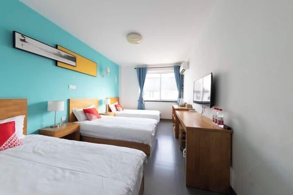 A hotel room with two beds, a desk, a TV, and a window with curtains.