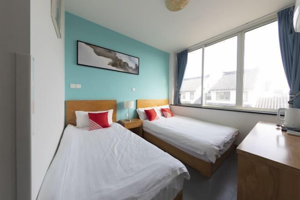 A hotel room with two beds, a desk, and a window with curtains.