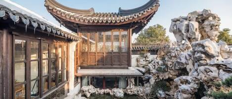 A traditional Chinese building with a curved roof, a pond, and rocky formations.