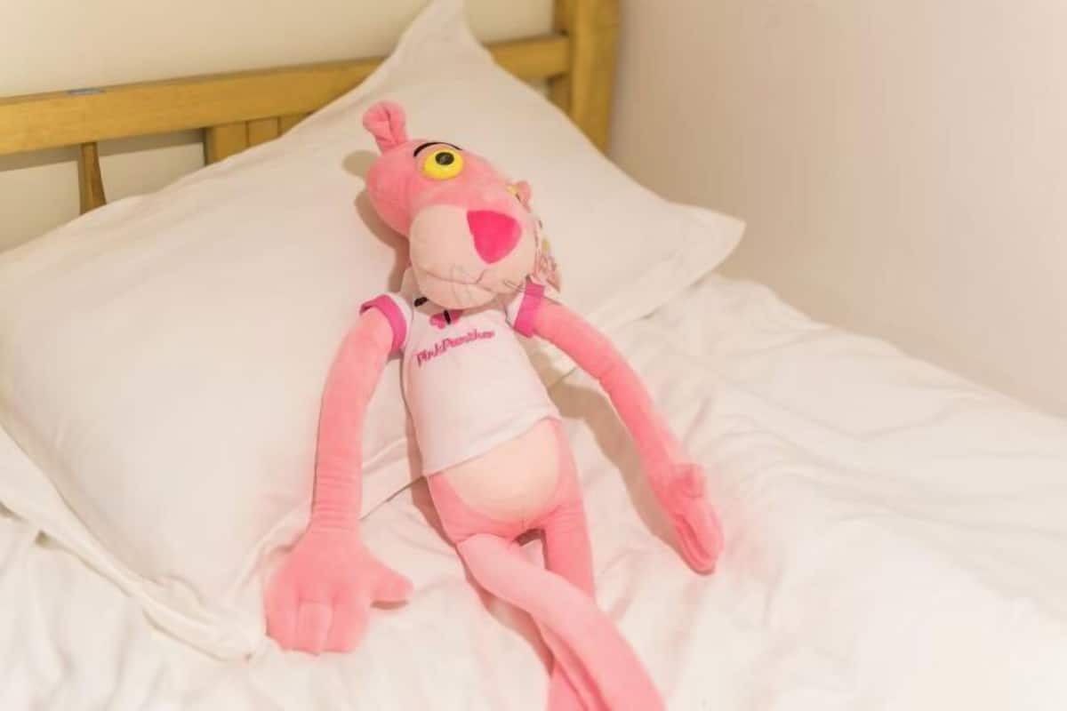 A plush toy on a bed with a wooden headboard.