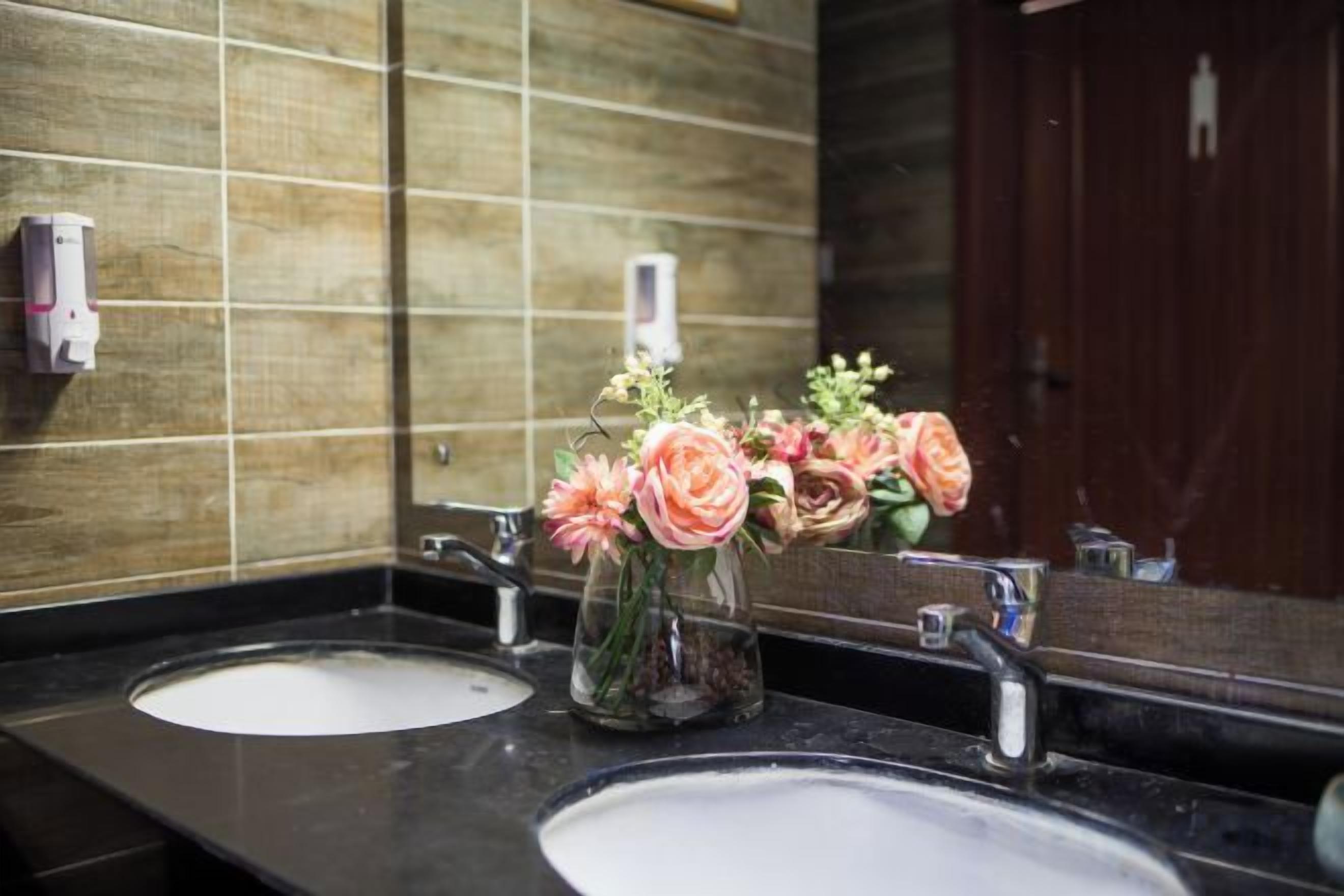A bathroom with two sinks, a mirror, and a vase with flowers.