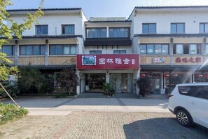 A building with a red sign indicating a restaurant and a parking area with a white car. - Yuanlin Hotel (Suzhou)