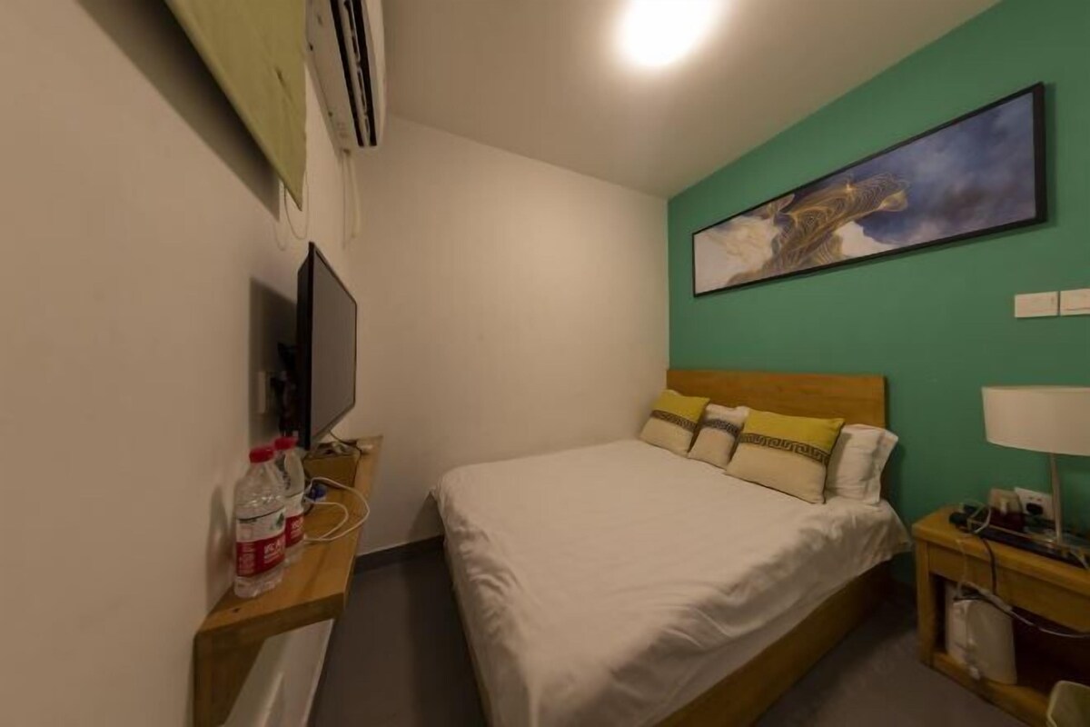 A hotel room with a bed, a TV, a painting on the wall, and a nightstand with a lamp.
