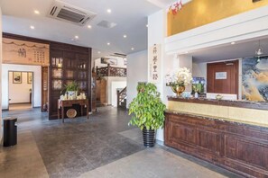 A hotel lobby with a reception desk, a staircase, and a large potted plant. - Yuanlin Hotel (Suzhou)