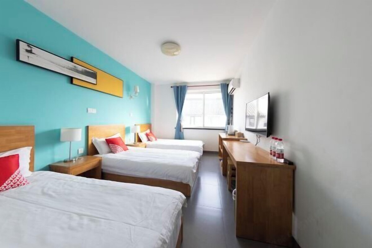 A hotel room with two beds, a desk, a television, and a window with curtains.