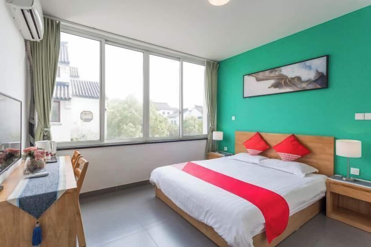 A hotel room with a bed, a desk, a chair, a window, and a painting on the wall.