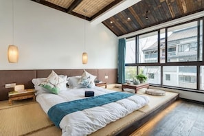 Une chambre avec un grand lit, des tables de chevet, une fenĂȘtre donnant sur un beau paysage et un plafond en bois.