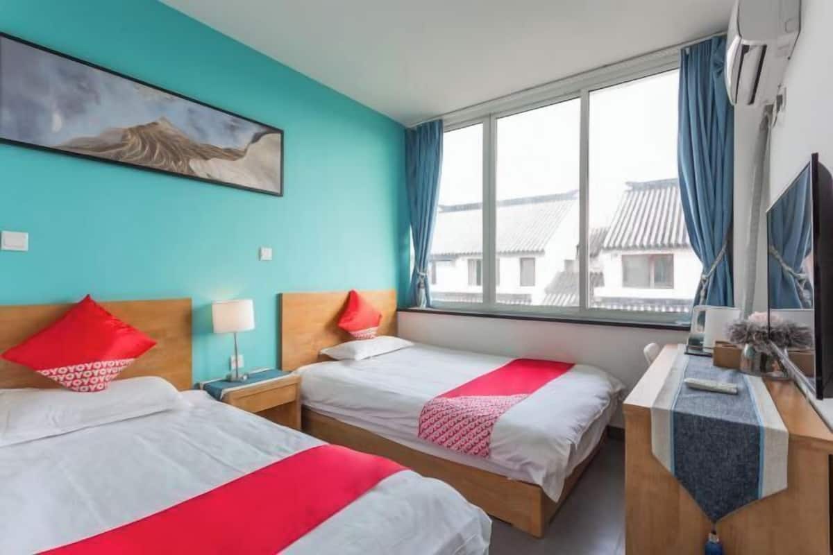 A hotel room with two beds, a desk, a TV, and a window with a view of traditional buildings.