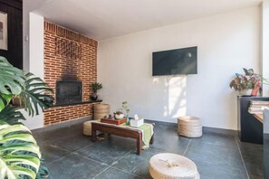 A living room with a brick fireplace, a flat-screen TV mounted on the wall, a bench, and a large plant. - Yuanlin Hotel (Suzhou)