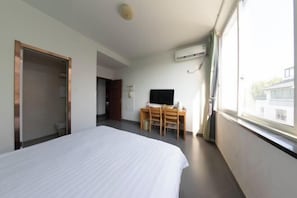 A hotel room with a bed, a desk with chairs, a TV, and a window with a view. - Yuanlin Hotel (Suzhou)