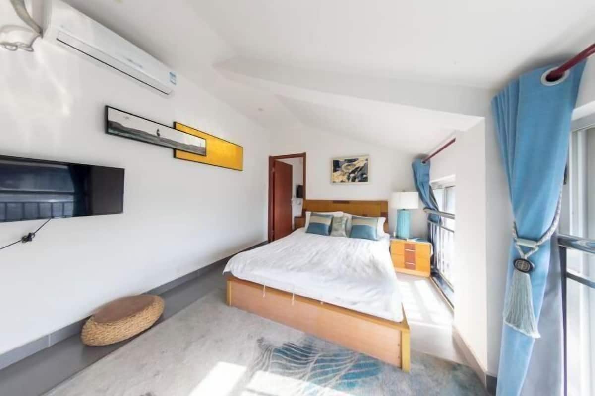 A bedroom with a bed, bedside table, lamp, and curtains.
