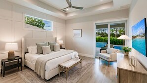 A modern bedroom with a large bed, a ceiling fan, a view of a swimming pool, and a large window. - Mimosa Manor Luxury Beach Home Heated Pool/Spa 4 Blocks From Beach (Naples)