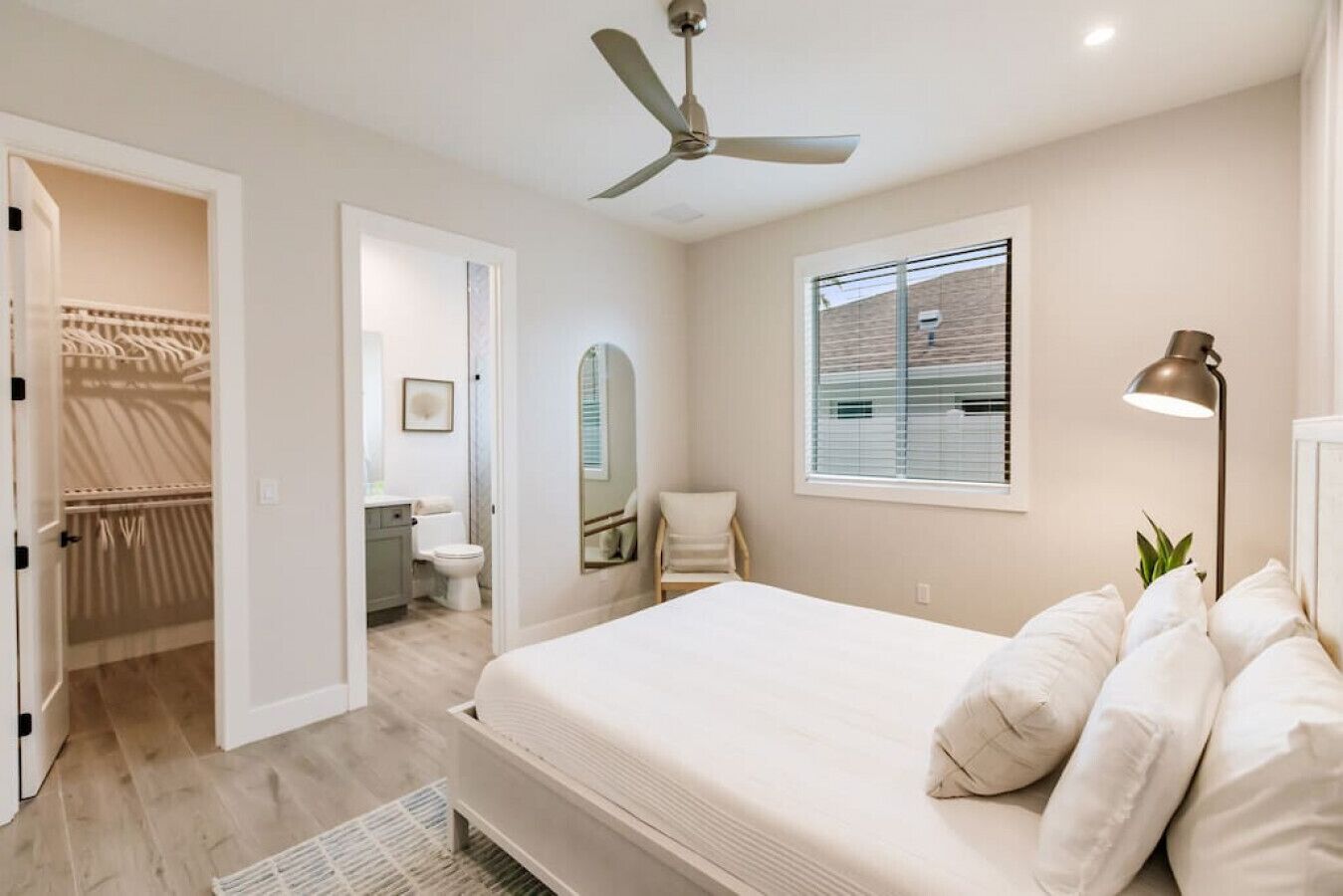 Un dormitorio con cama, ventilador de techo, ventana con persianas y lámpara de noche, con vistas al exterior.