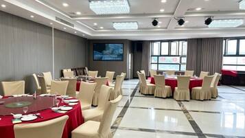 Un salón de conferencias con mesas redondas, sillas, una pantalla grande y vista al mar.