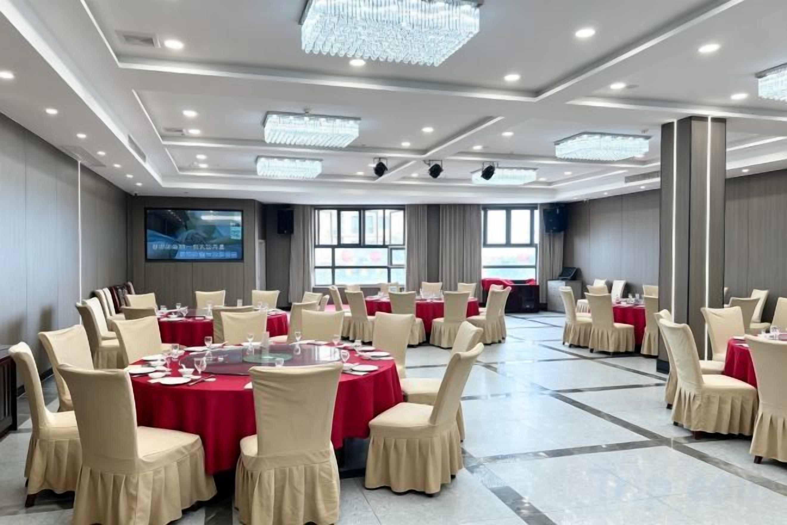Un salón de conferencias con mesas redondas, sillas, una pantalla grande y un candelabro.