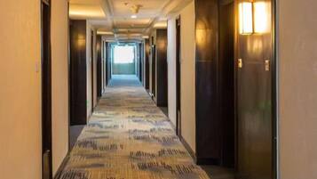 A hotel hallway with a patterned carpet, doors on both sides, and wall-mounted light fixtures.