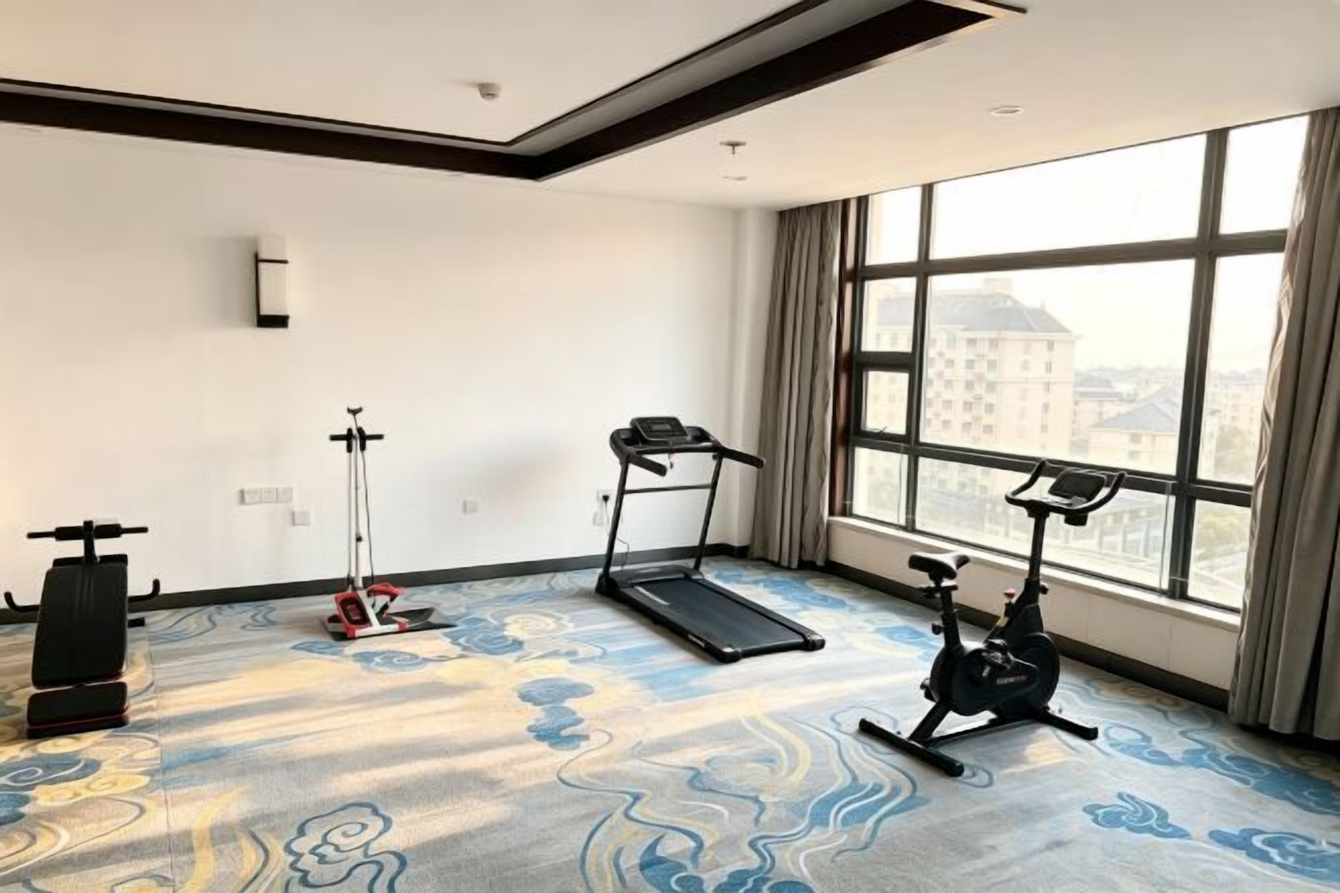 A hotel room with a large window, a treadmill, an exercise bike, and a stationary bike.