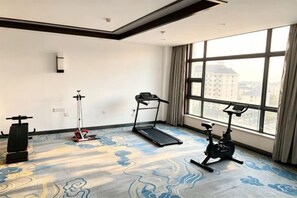 Habitación de hotel con un ventanal grande, una cinta caminadora, una bicicleta estática y una bicicleta elíptica.