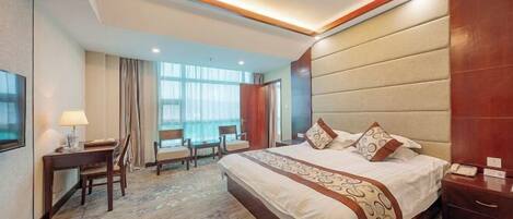 A hotel room with a large bed, a desk, chairs, a TV, and a window with curtains.