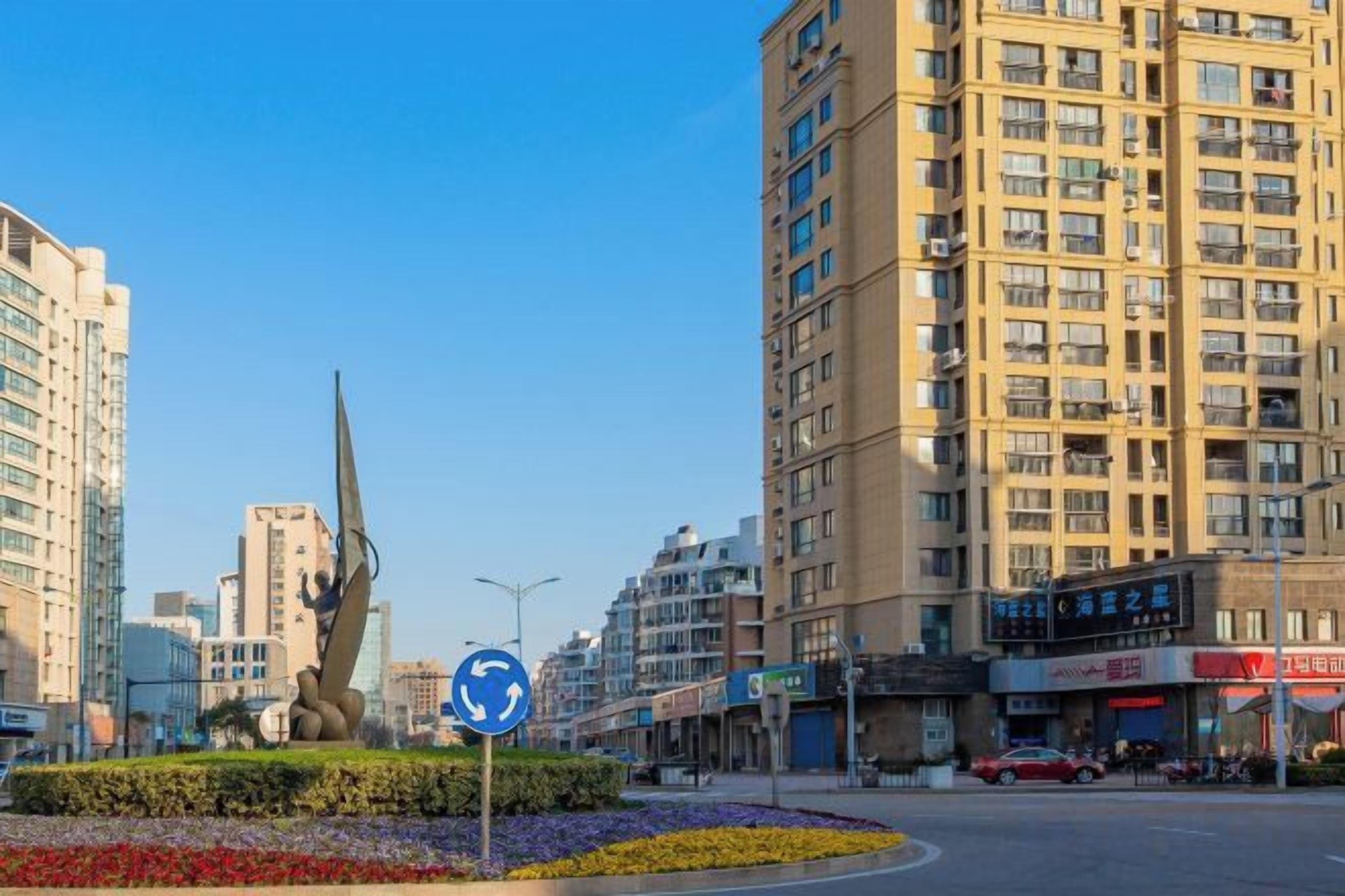 A city street with tall buildings, a roundabout, and a sculpture.