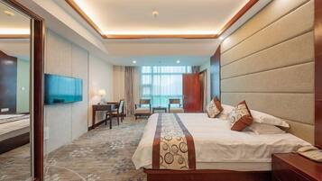 A hotel room with a large bed, a desk with a chair, a TV, and a window with curtains.