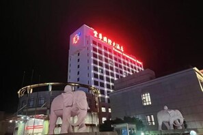 Un hotel con un edificio destacado, señalización iluminada, una estructura circular con una estatua y una gran escultura de elefante.