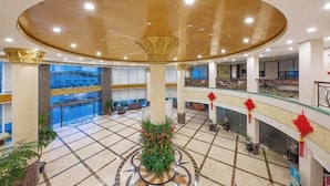A spacious atrium with a high ceiling, multiple levels, and a central decorative plant arrangement.