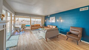 Ein geräumiges Wohnzimmer mit großem Fenster, blauer Akzentwand und Holzboden.