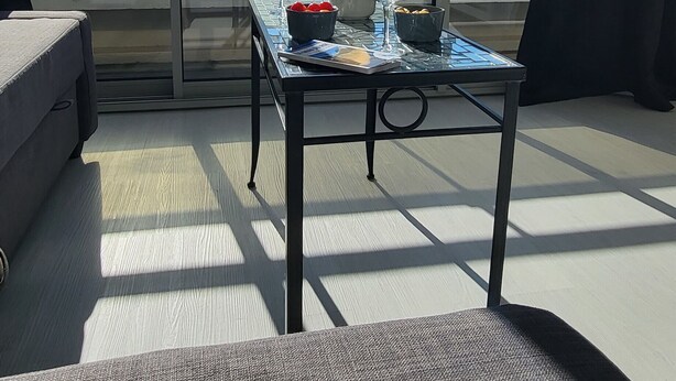 Un balcón con una mesa lista para dos personas, con una botella, copas y un cuenco de fruta.