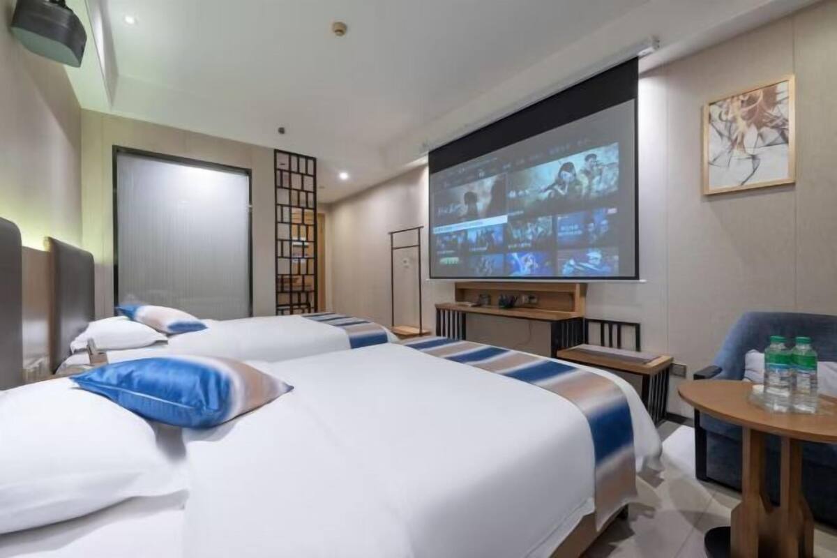 Une chambre d’hôtel avec deux lits, un écran de télévision diffusant plusieurs chaînes, un bureau en bois et une chaise.